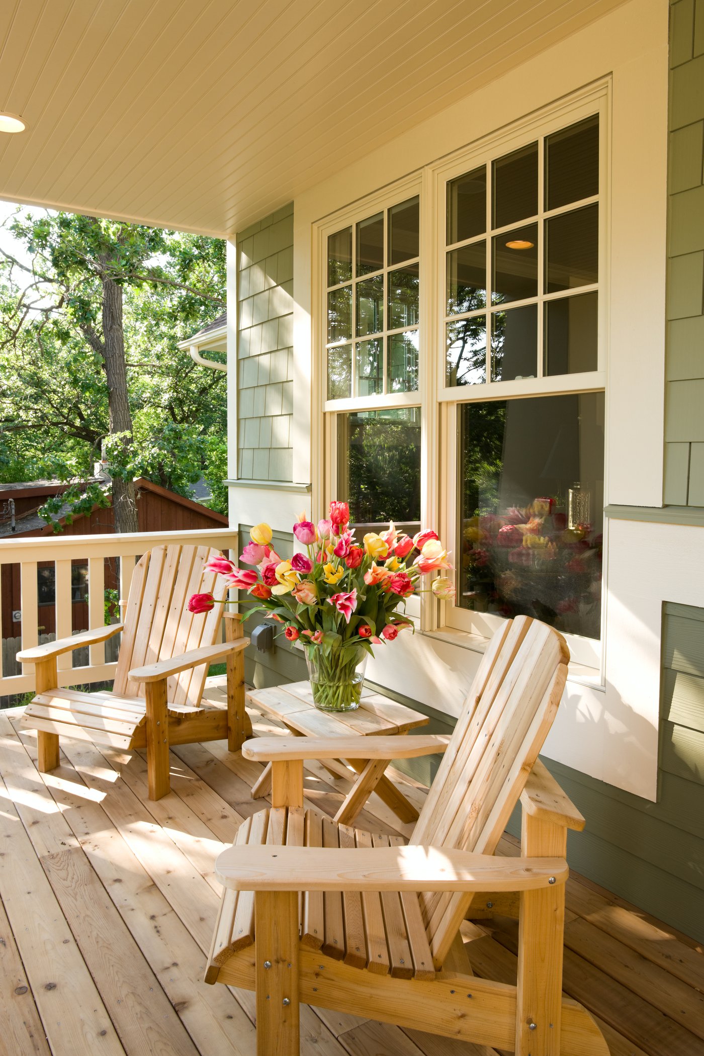Sunlit covered front porch with cedar chairs and fresh tulips